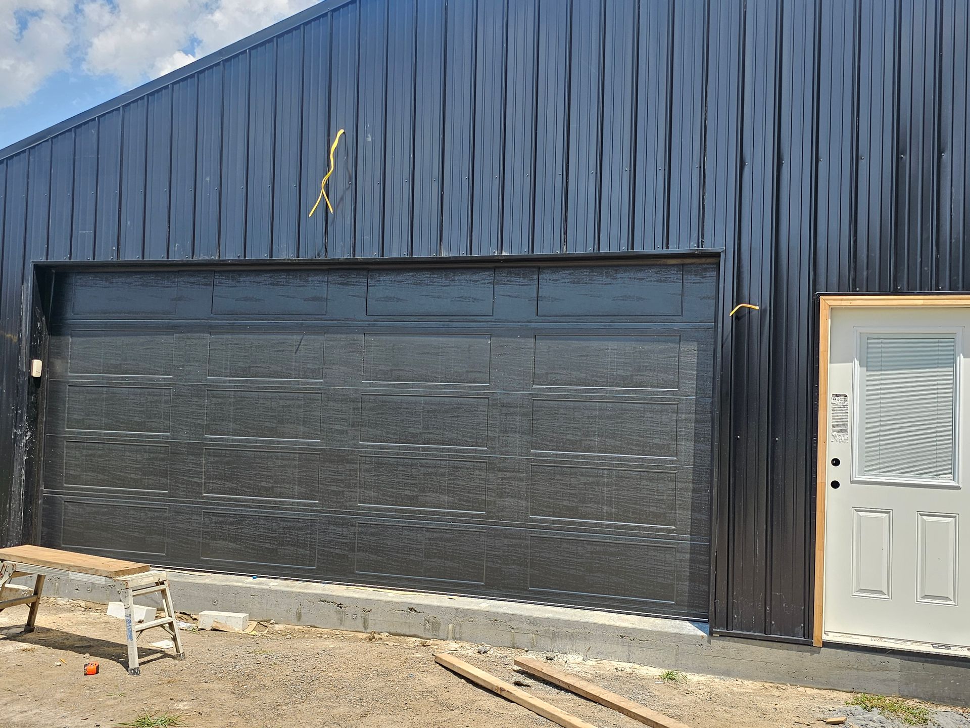 A black garage door is being installed on the side of a building.