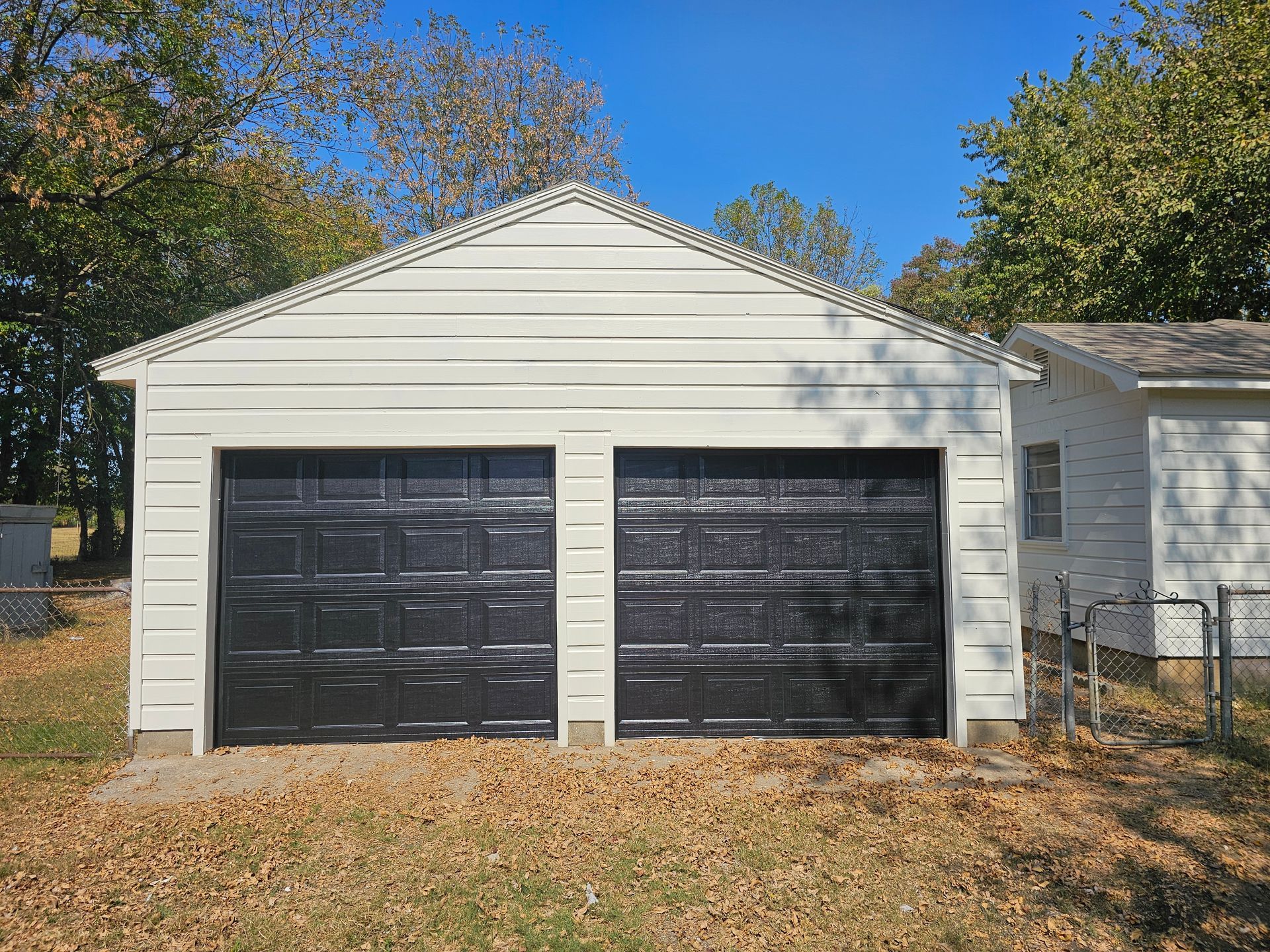 A white garage with black garage doors is next to a house.