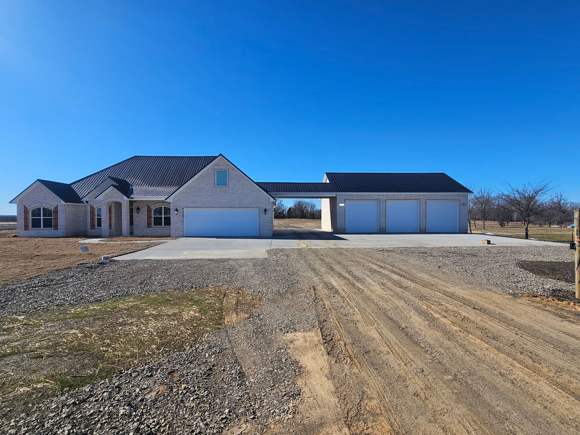 A large house with three garages is sitting on top of a dirt field.