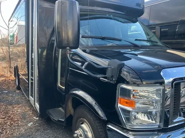 A close-up view of the front passenger side of a black shuttle bus parked on a gravel lot.