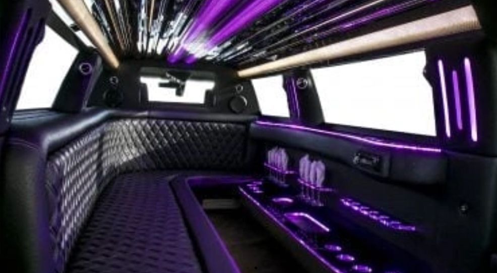 Interior of a black limousine with purple LED lights, quilted leather seating, and bar area.