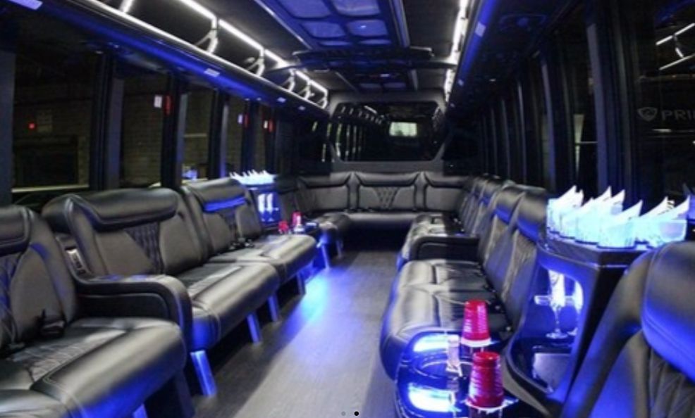 Interior of a party bus with black leather seating, ambient blue lighting, and drink holders.