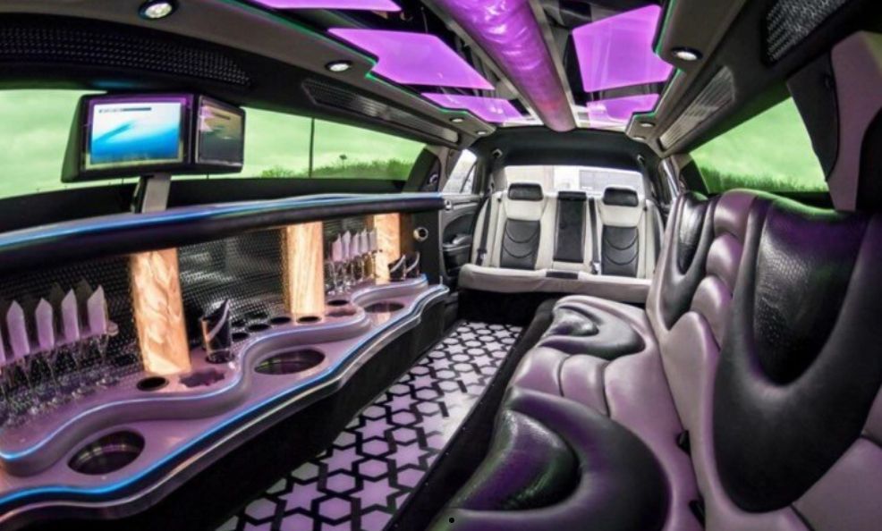 Interior of a limousine. Black, white, and purple color scheme. Bar, TV, and seating.