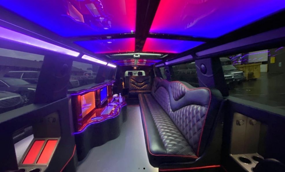 Interior of a limousine with red and blue ceiling lights, black leather seating, and multiple screens.