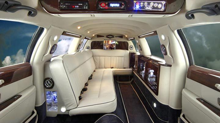 Interior of a white limousine with white leather seats, dark wood accents, and ambient lighting.