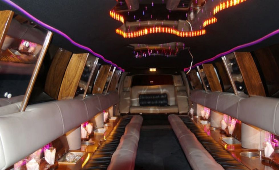 Interior view of a limousine with mirrored accents, wooden panels, and purple and orange lighting.