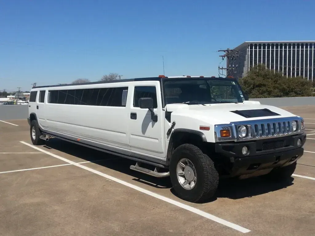 White Hummer limousine parked in an outdoor lot on a sunny day.