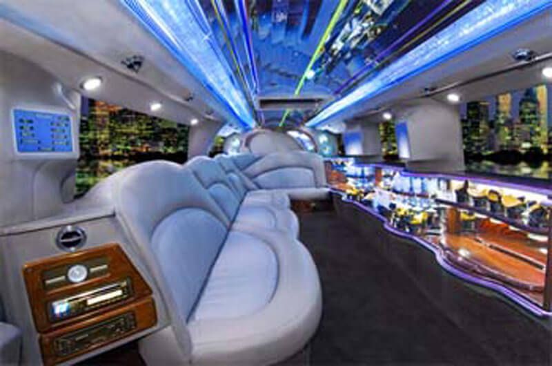 Interior of a luxurious limousine with blue and white seating, bar, and city skyline view.