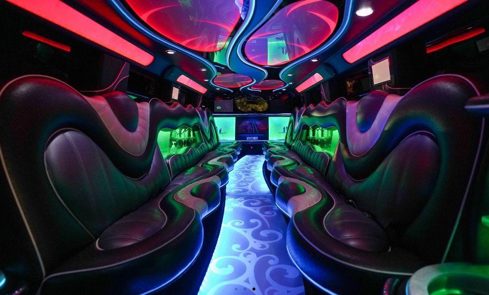 Interior of a party bus with leather seating, neon lights in blue, green, and red, and a patterned floor.