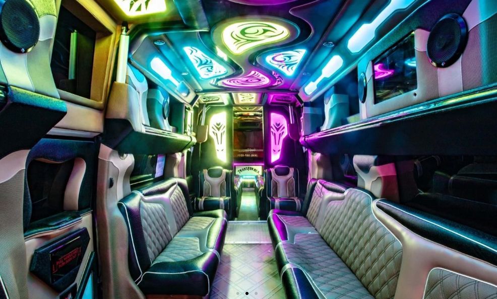 Interior of a party bus with neon lighting, black and grey seating, and built-in speakers and screens.