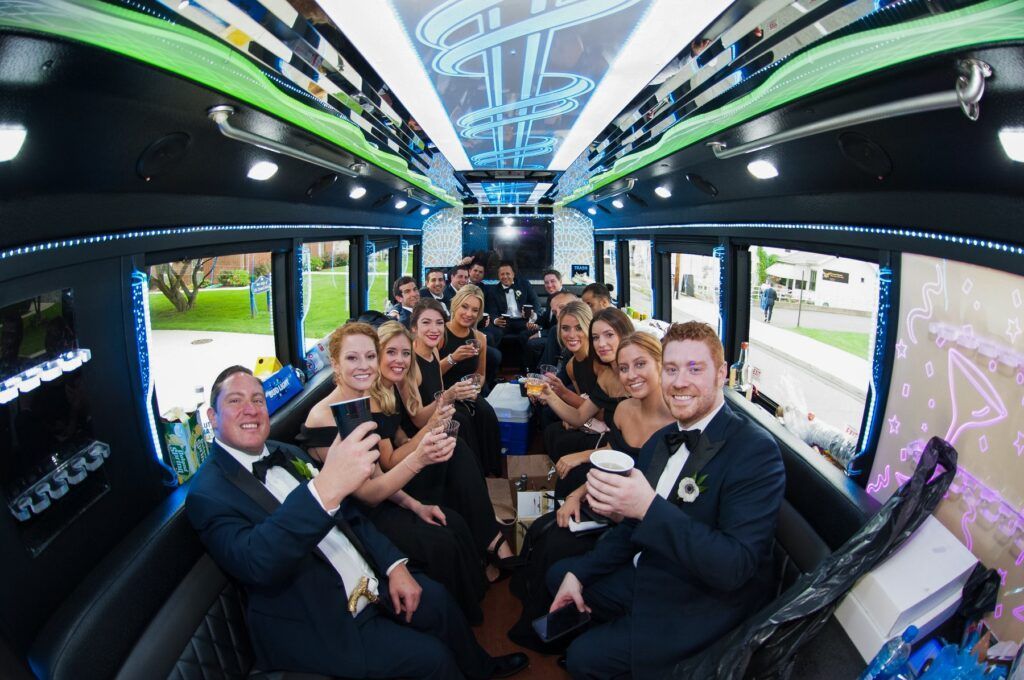 People in formal attire inside a limousine, toasting and smiling. Black interior with neon lights.