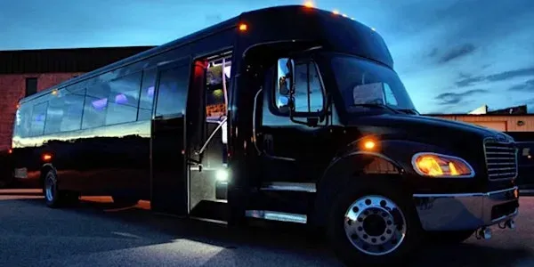 Black party bus with door open, illuminated, under a twilight sky.
