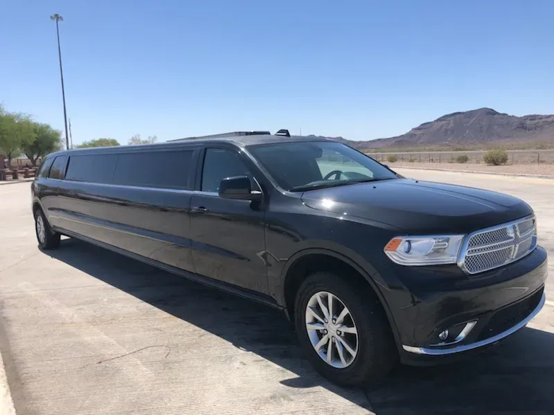 Black Dodge Durango limousine parked on a paved lot on a sunny day with a mountain in the background.