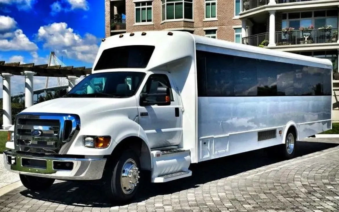 White party bus parked on a cobblestone road, in front of a modern building with a blue sky.