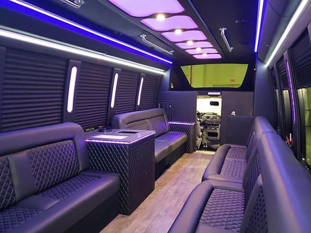 Interior of a luxury black van with leather seating, ambient purple lighting, and shades.