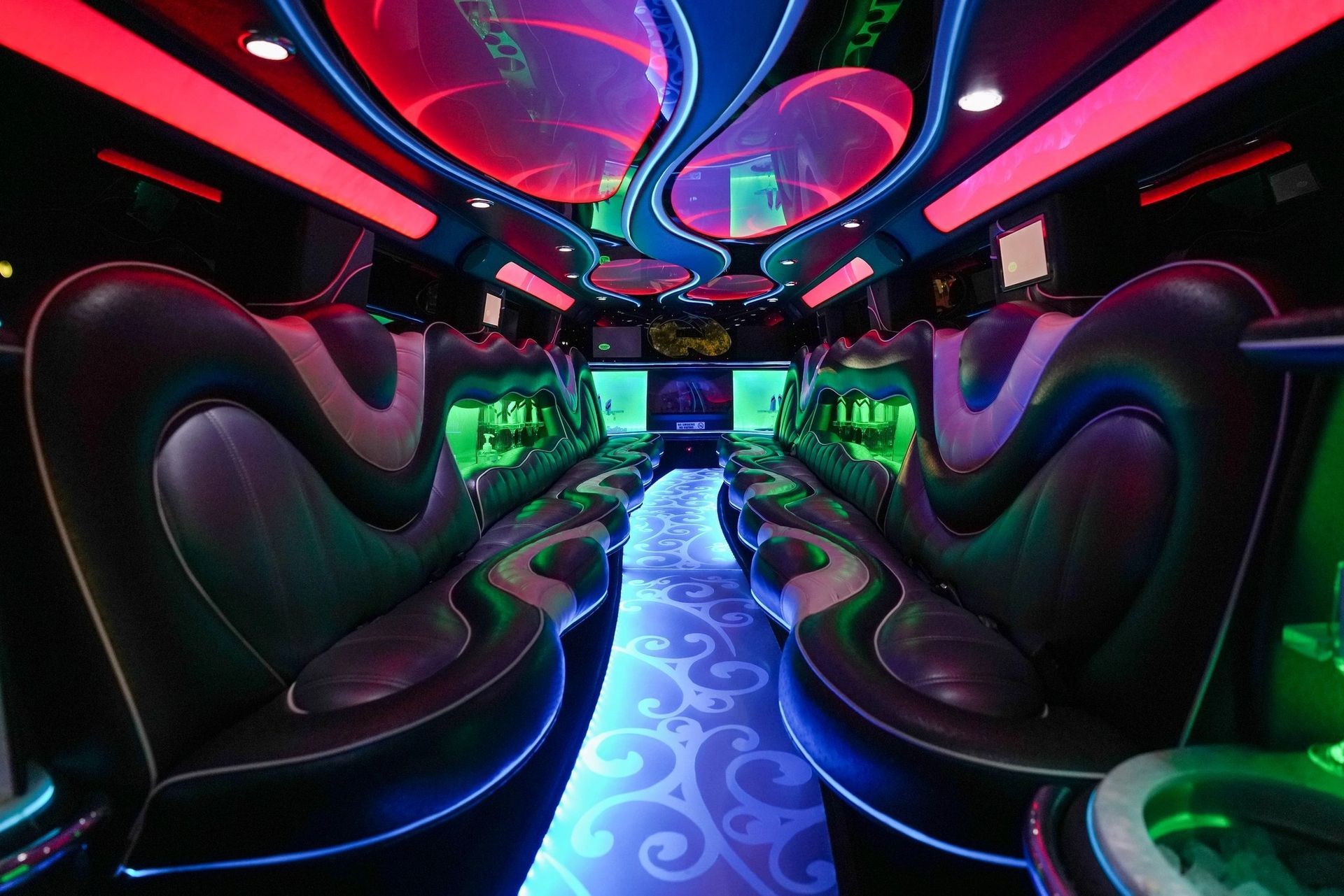 Interior of a limousine with black leather seating, colorful LED lighting and a patterned floor.