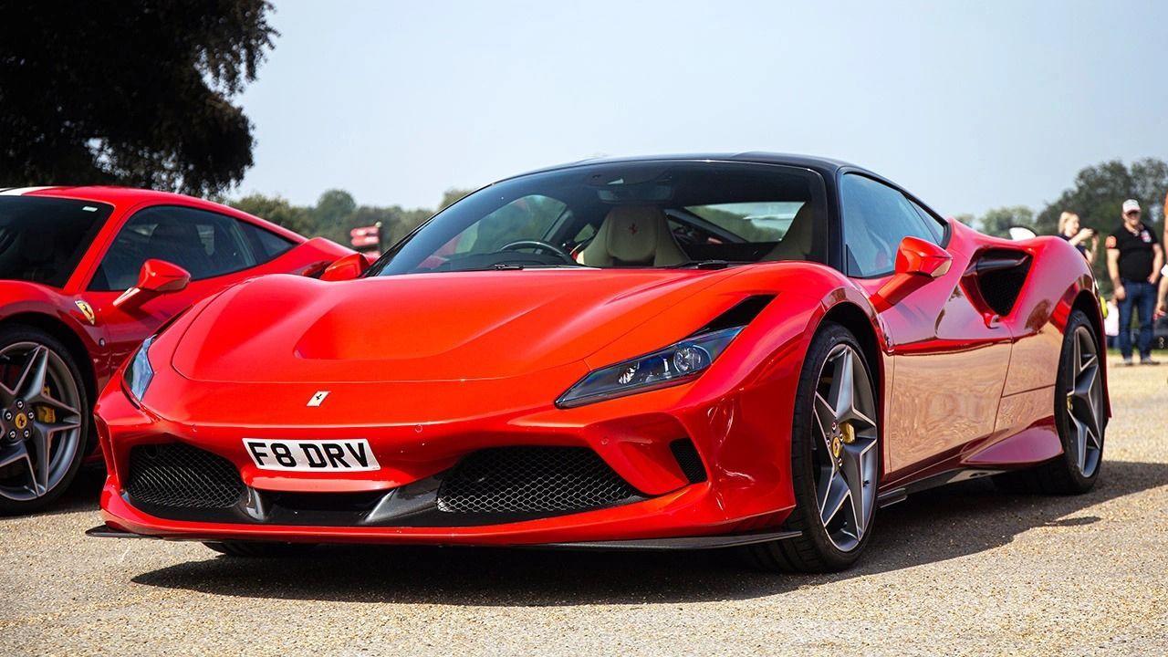 Red Ferrari sports car with black roof, parked outside on a sunny day.