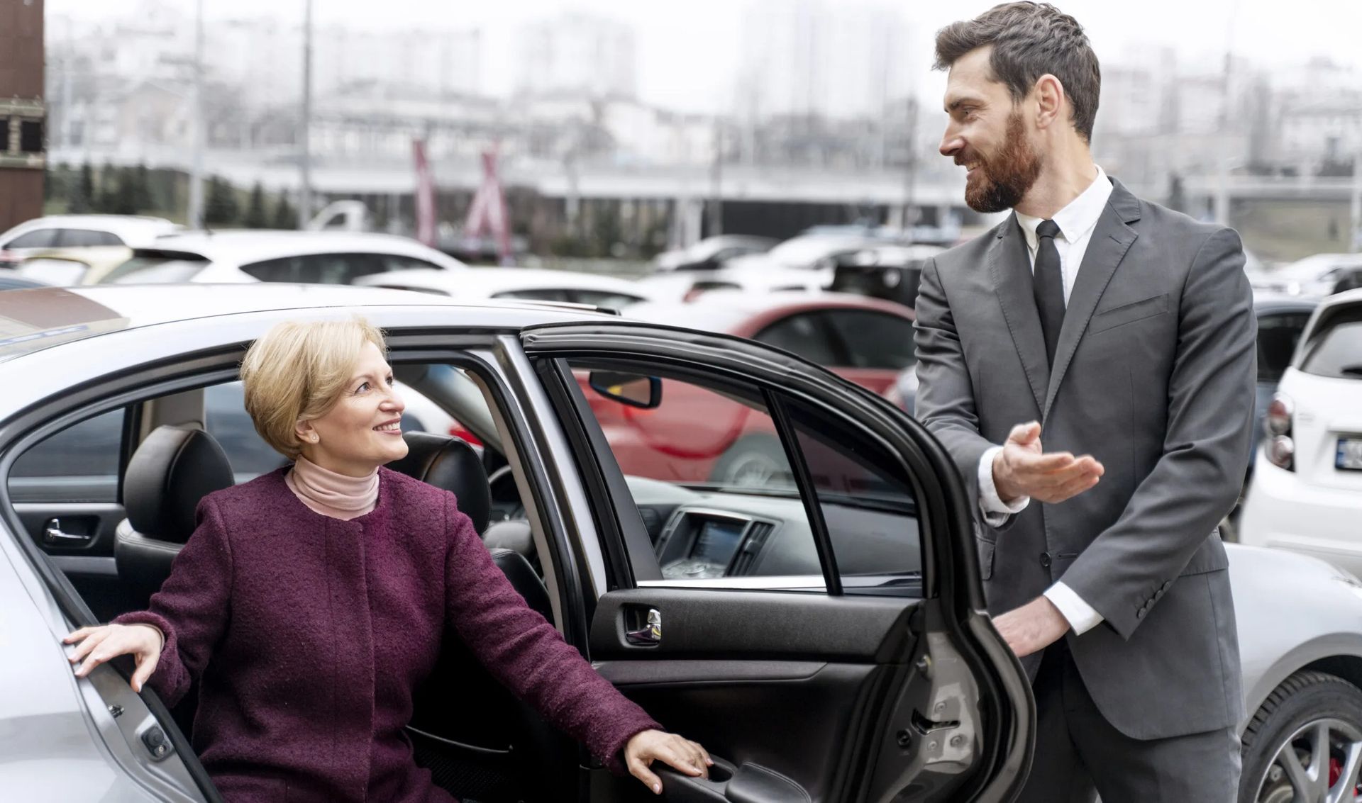 Man in suit assisting woman exiting car in parking lot.