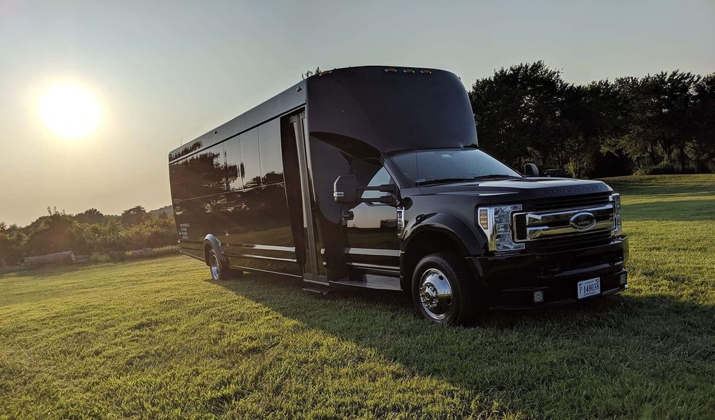 Black party bus parked in a grassy field at sunset.