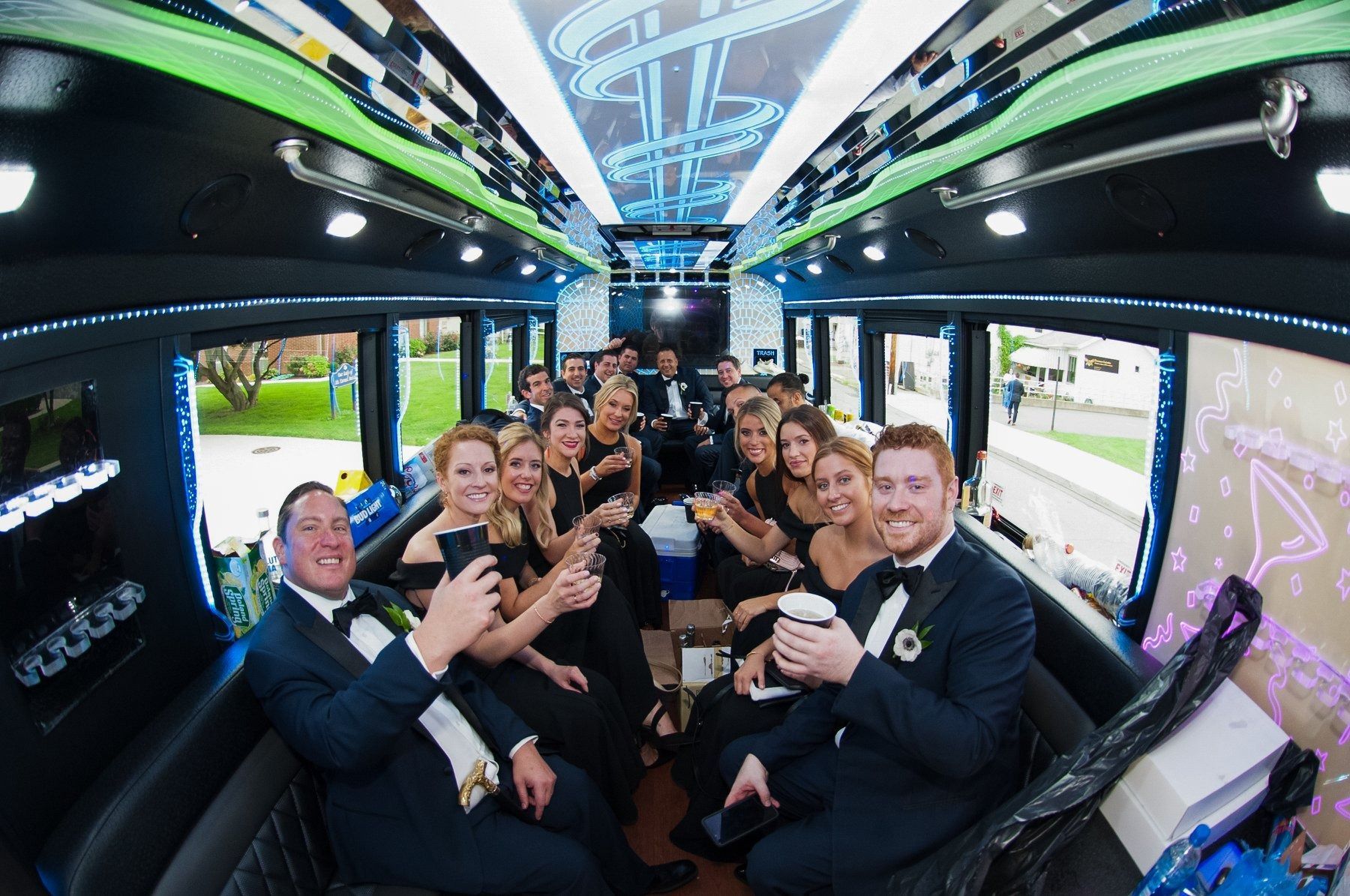 Group of people in formal attire inside a party bus, toasting drinks, celebrating with smiles.