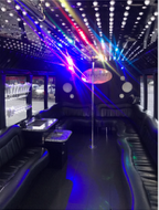 Interior of a party bus with a dance pole, seating, tables, and colorful lights.