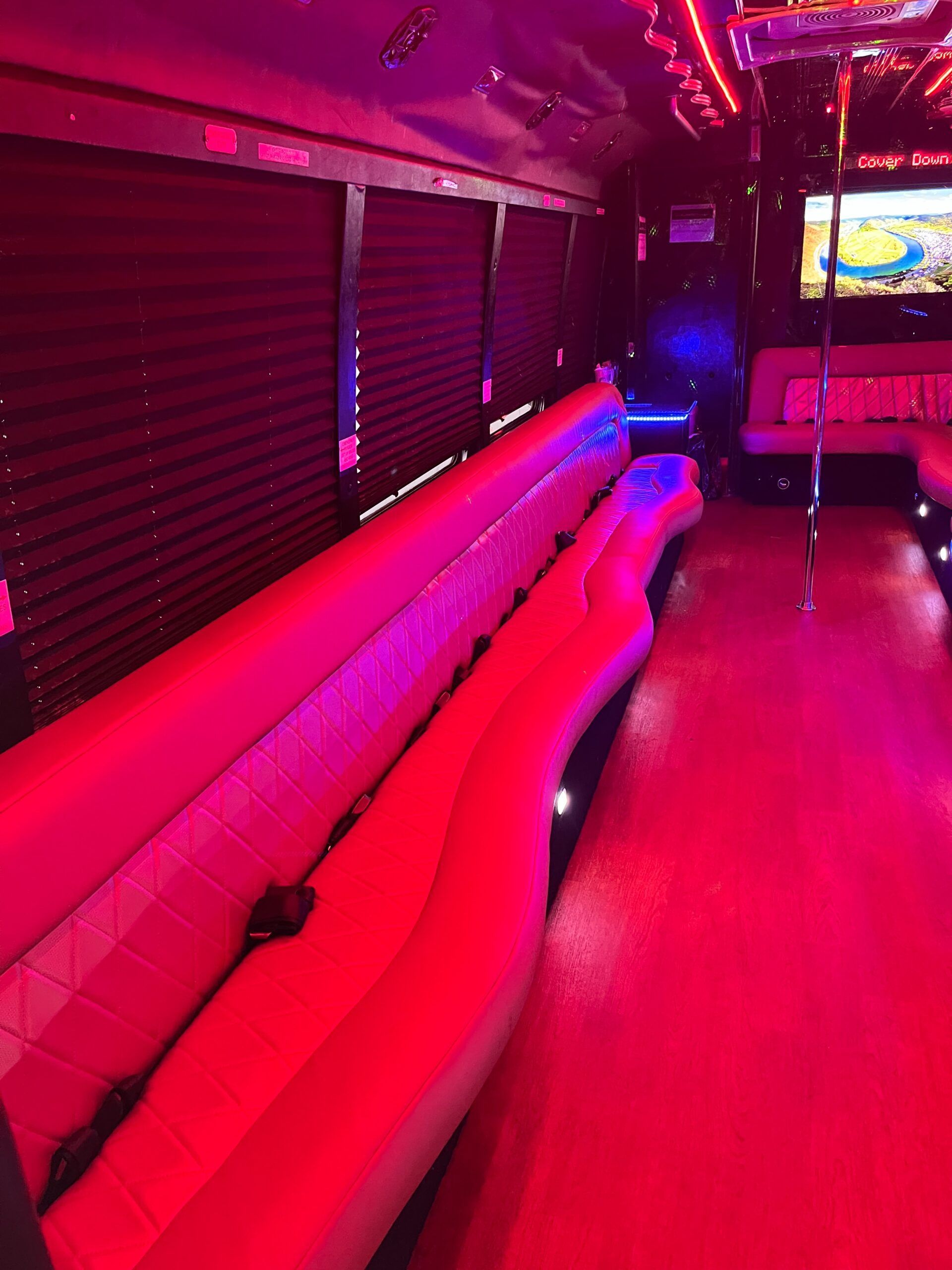 Interior of a party bus with red and purple lights, leather seating, and a pole.