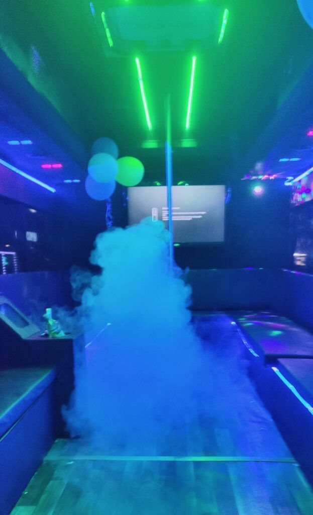 Dark room with blue and green neon lights, smoke, a projection screen, and balloons.