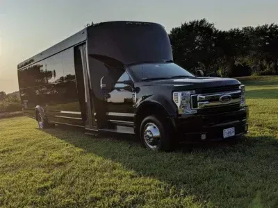Black party bus on grass, parked outdoors. Sunlight illuminates the front.