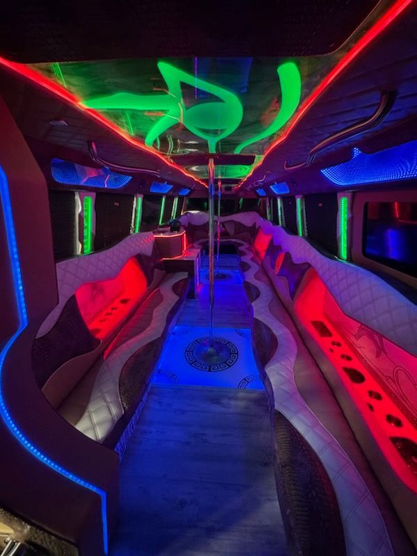 Inside a party bus with colorful neon lighting and a central dance pole.