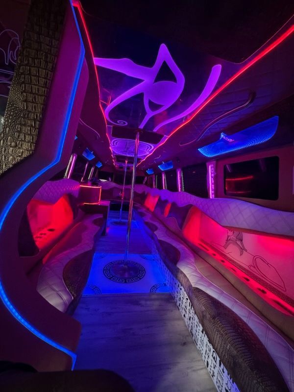 Interior of a party bus with neon lights. Red, blue and purple lights illuminate seats, ceiling, and dance pole.