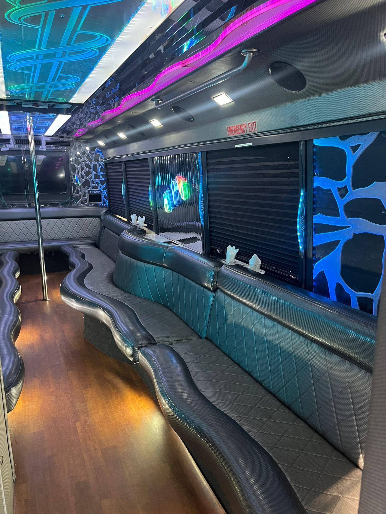 Interior of a party bus with black quilted leather seating, wood flooring, and neon lighting on the ceiling.