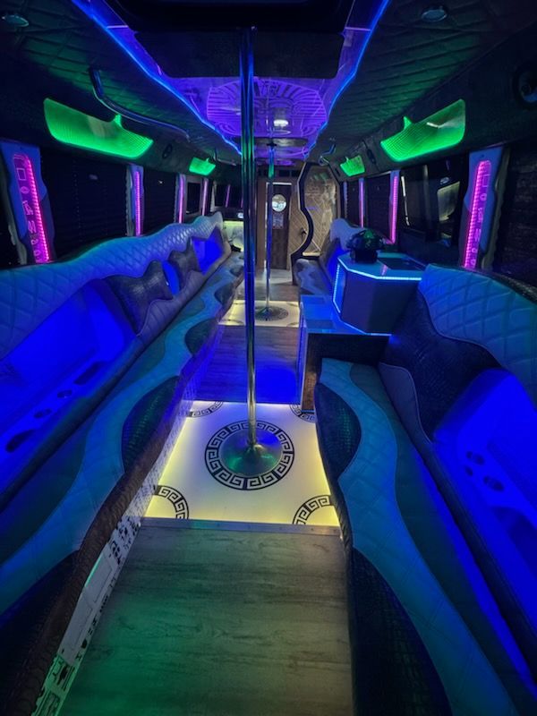 Interior of a party bus with blue, green, and pink LED lighting. Seats face each other around a central pole.