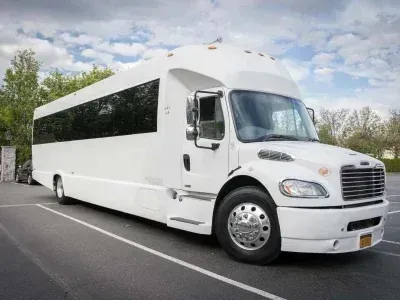 White party bus parked on an asphalt lot; cloudy sky background.