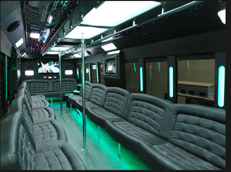 Interior of a party bus: black seating, neon green lights, mirrored ceiling, TV screens, and a central pole.