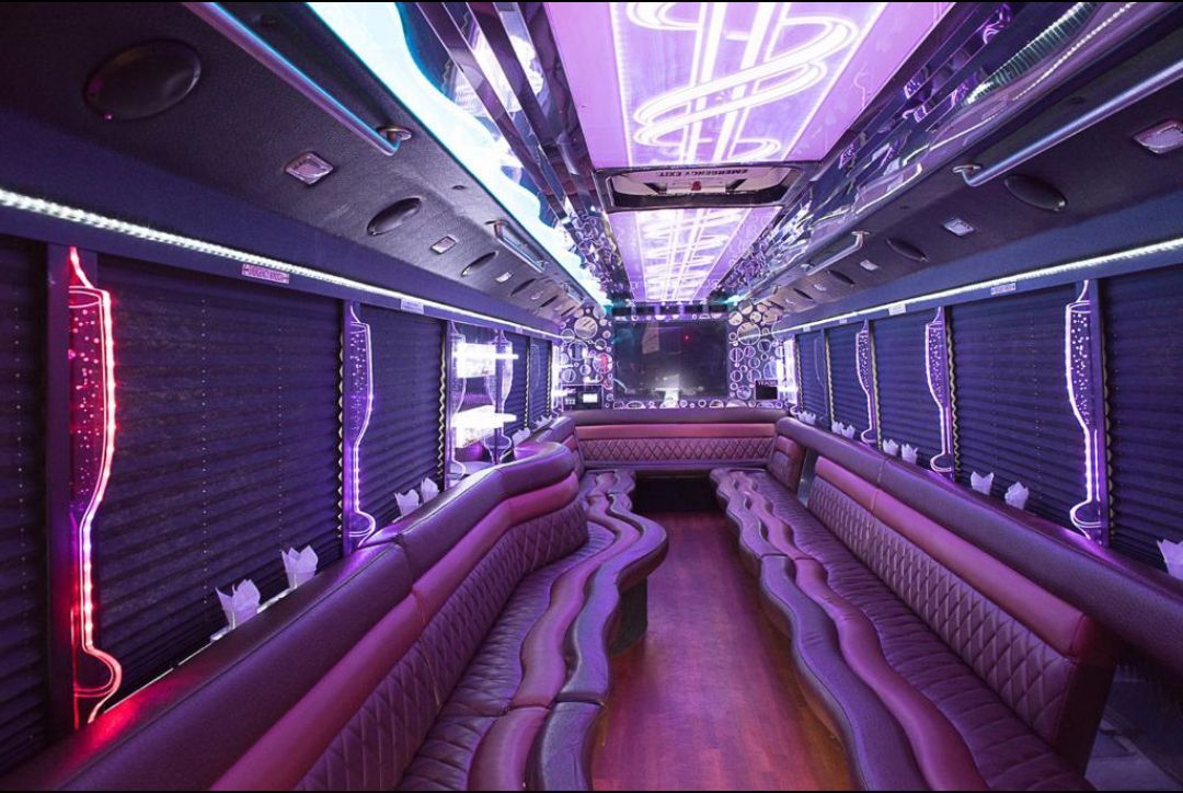 Interior of a limousine with purple lighting, seating, and a decorative ceiling.
