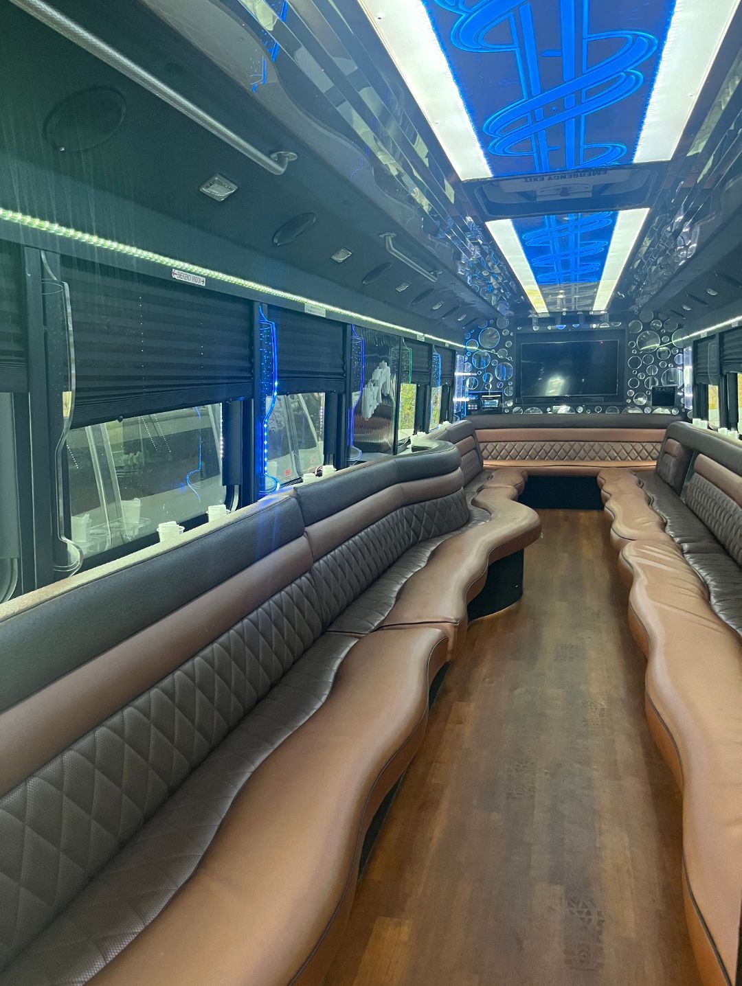 Interior of a luxury party bus with brown leather seating, wood floor, and blue LED lighting.