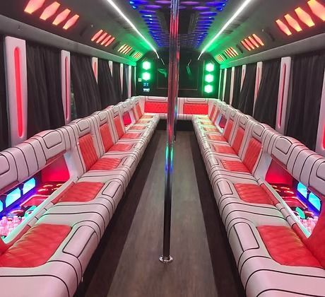 Interior of a party bus with red and white seating, a pole, and colorful LED lighting.