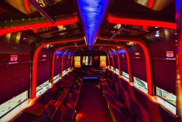 Interior of a party bus with red and blue neon lights, rows of seats, and a mirrored ceiling.
