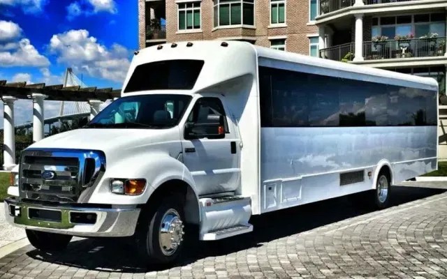 White party bus parked on a cobblestone road, in front of a modern building with a blue sky.