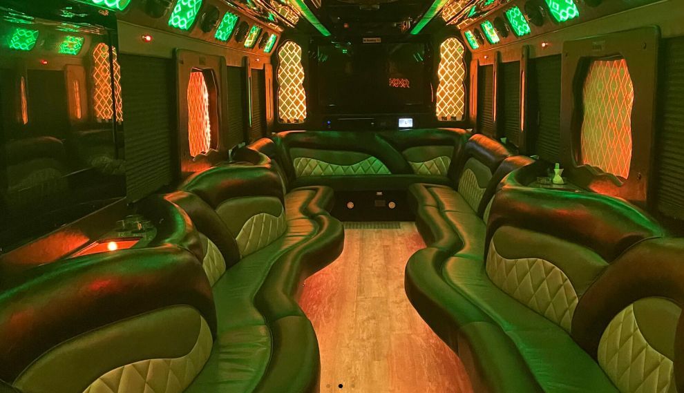 Interior of a limousine with green and orange lighting, seating along the walls, and a wooden floor.
