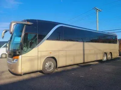 Tan and black passenger bus parked on asphalt. Clear blue sky in the background.