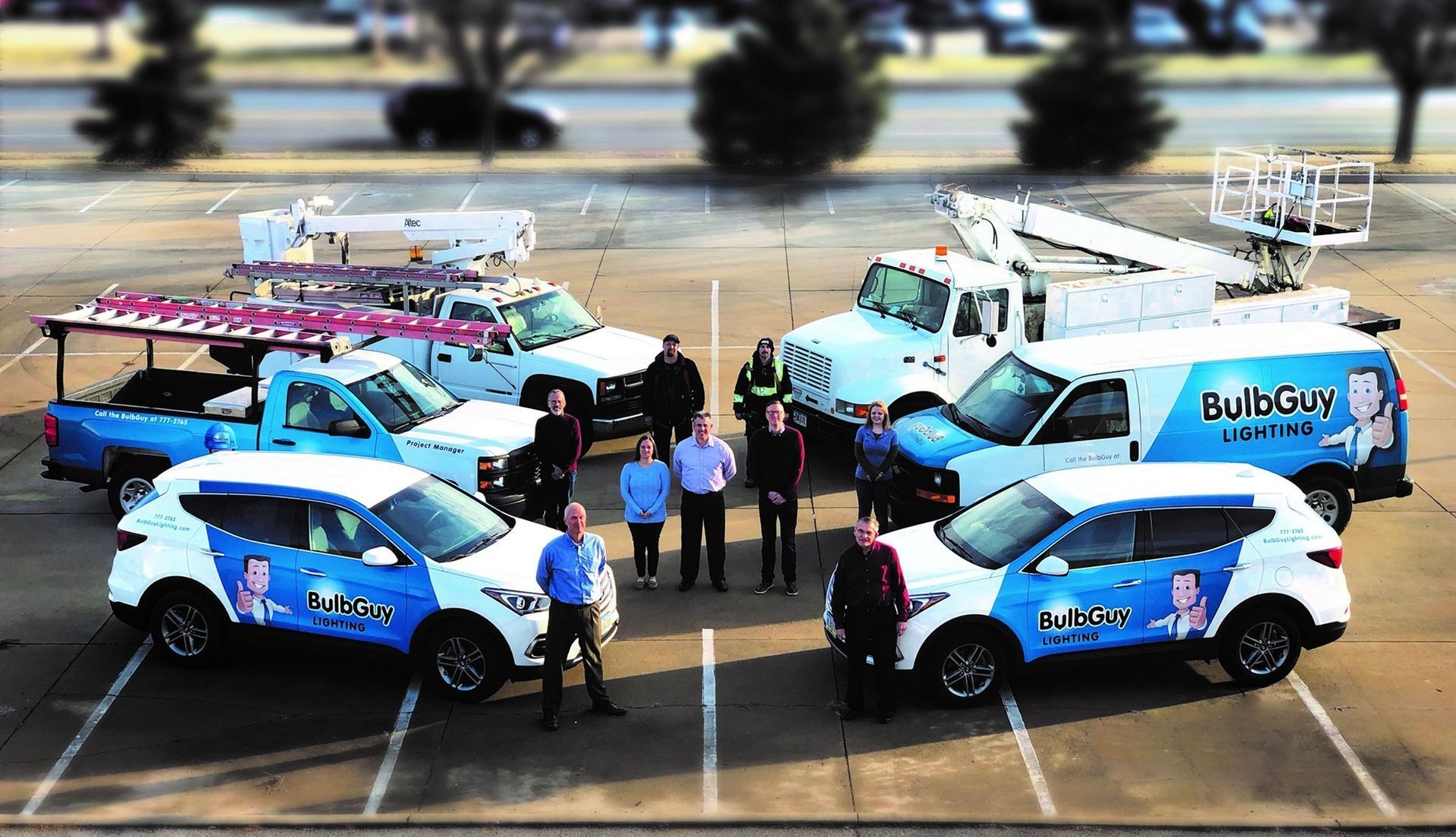 Team and vehicles of "Big Dog" company in parking lot. Trucks and SUVs; blue, white, and pink.
