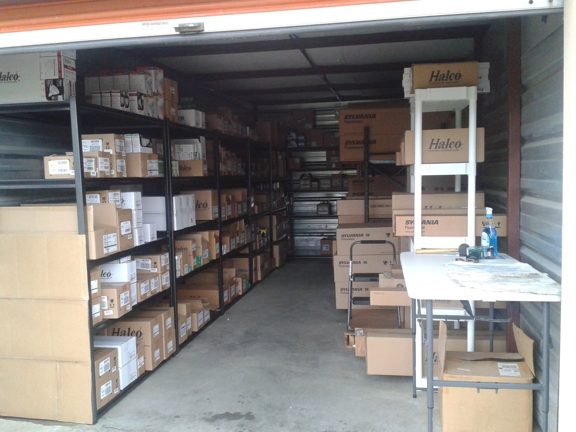 Storage unit filled with shelves and boxes, a work table on the right.