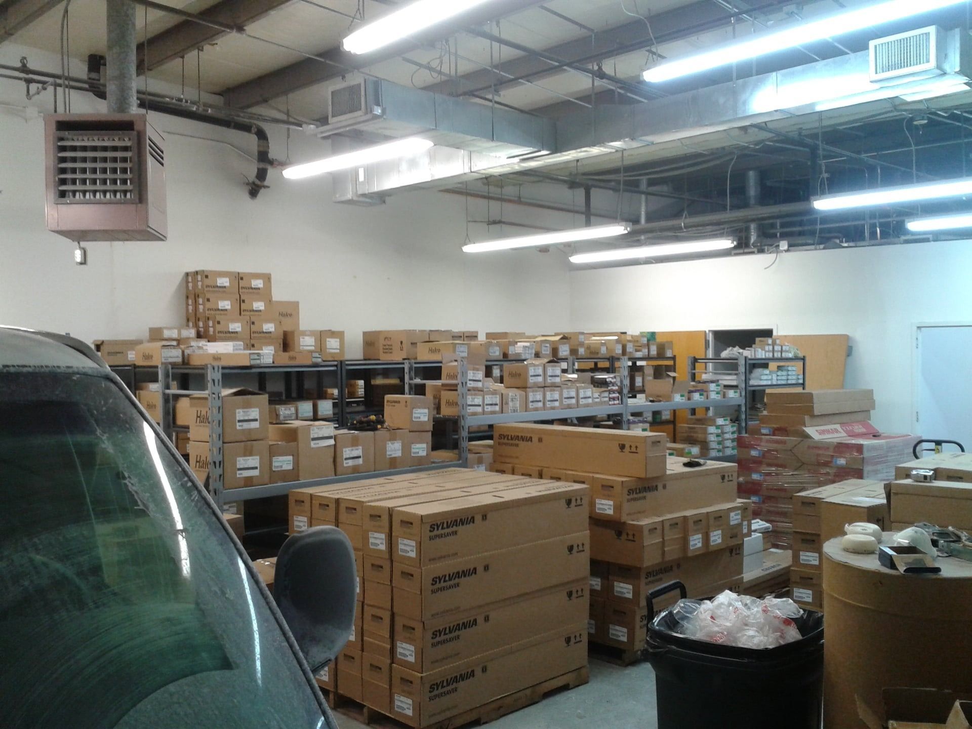 Warehouse interior with boxes on shelves. A truck's windshield is in the foreground.