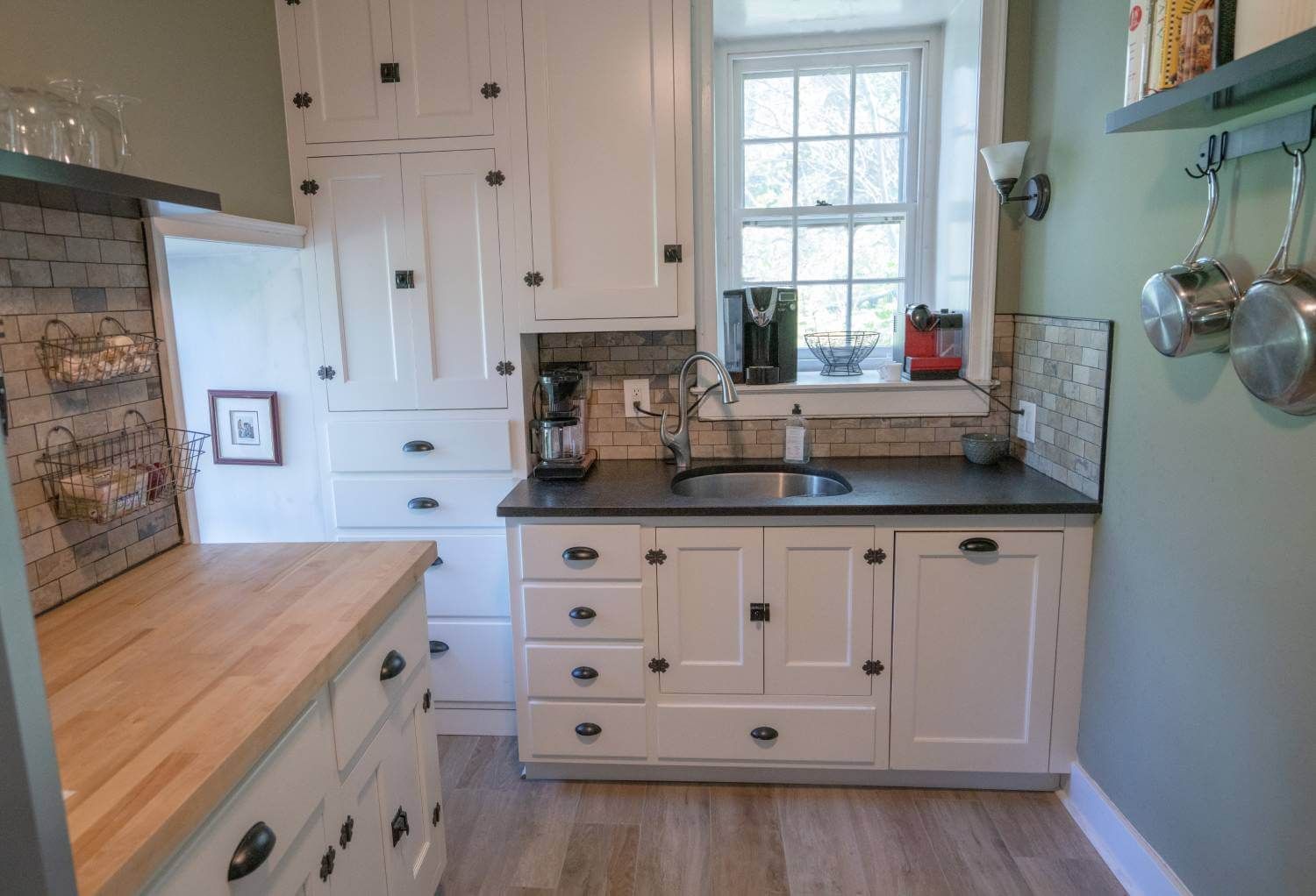 A kitchen with white cabinets, wooden counter tops, a sink and a window