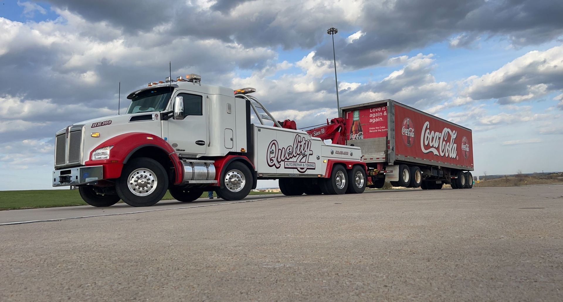 A white and red tow truck is towing a coca cola trailer.