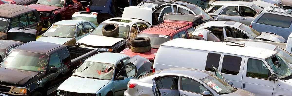 Cars piled up in a junkyard. Various colors and models with damaged parts fill the frame.