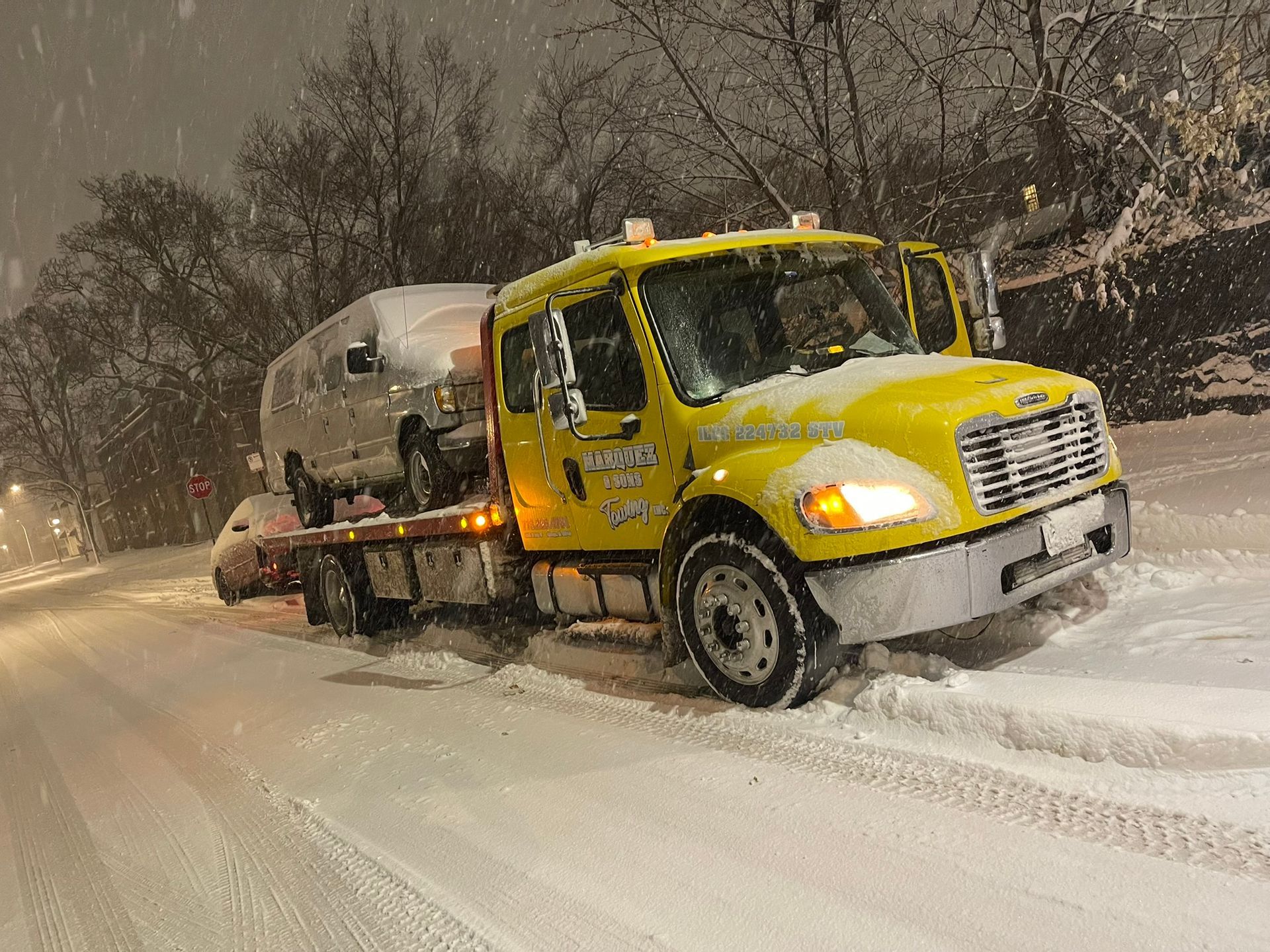 Yellow tow truck hauling a van on a snow-covered road at night.