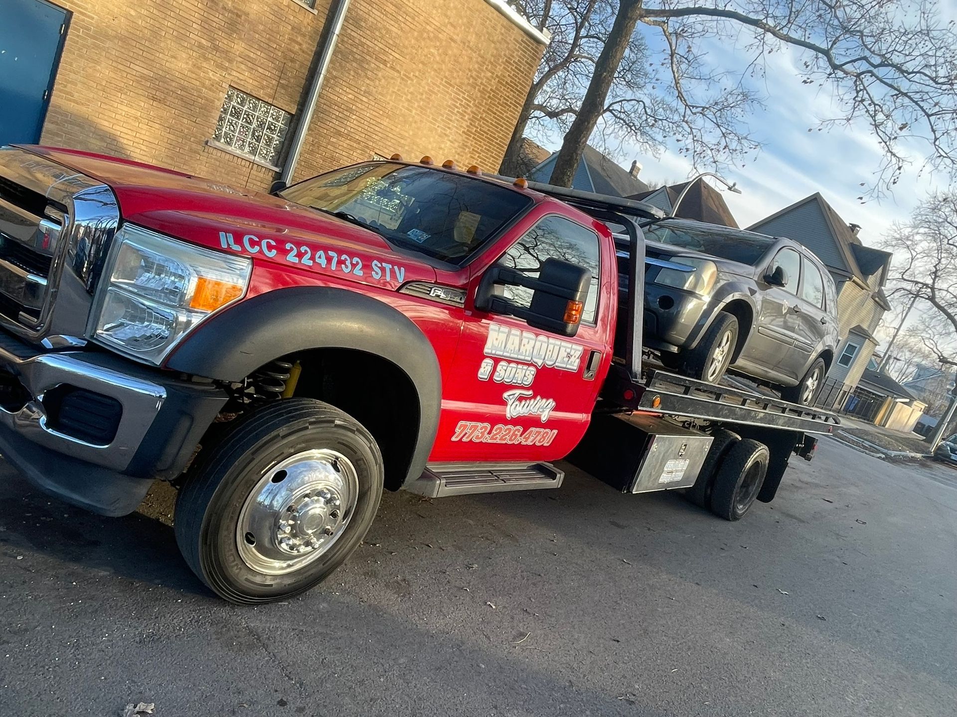 Red tow truck hauling a gray SUV on a city street.