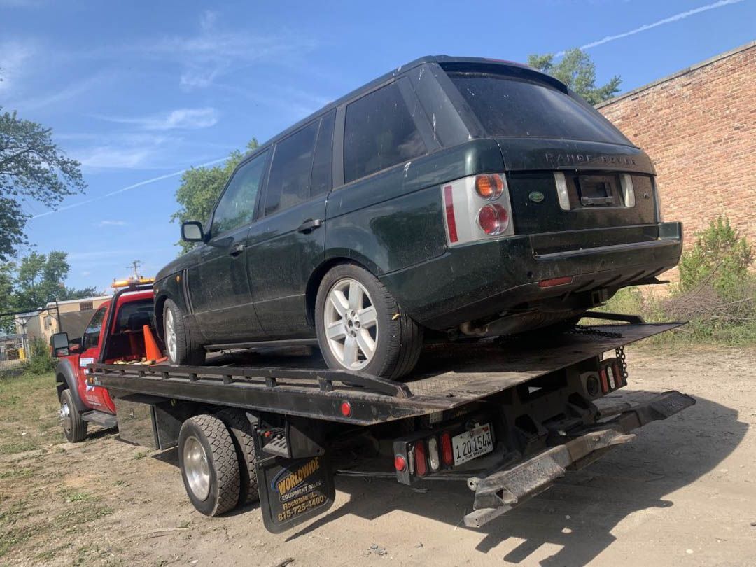 Dark green SUV on a flatbed tow truck on a sunny day.